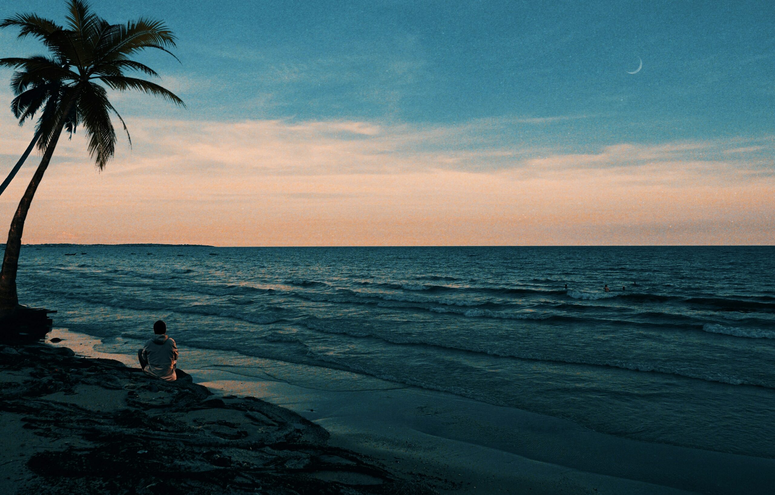 Person sitting alone on a quiet beach at sunset, reflecting during an intentional travel experience